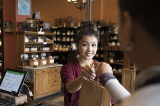 A young woman takes a bag of purchased items from cashier at the register counter.