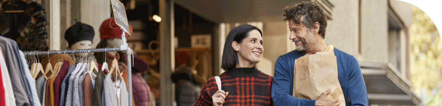 A couple smiling and walking with shopping bags outside a clothing store
