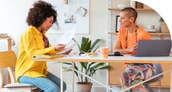 Two women sitting at a desk in an office, discussing documents