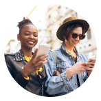 Two women smiling and using their mobile while walking